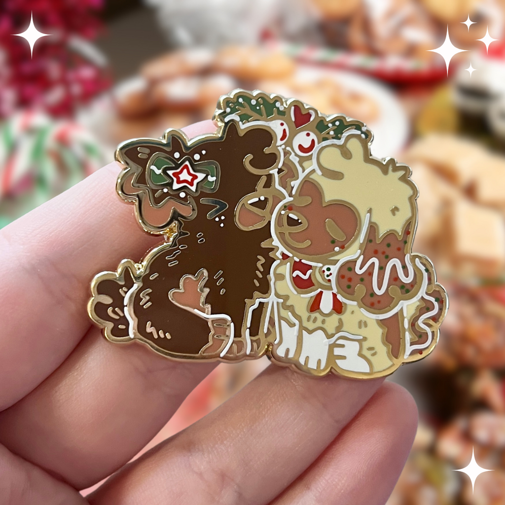 an enamel pin featuring Cinnamon, the Gingersnap puppy, and Caramel, the Sugar Cookie puppy, sharing a sweet mistletoe kiss