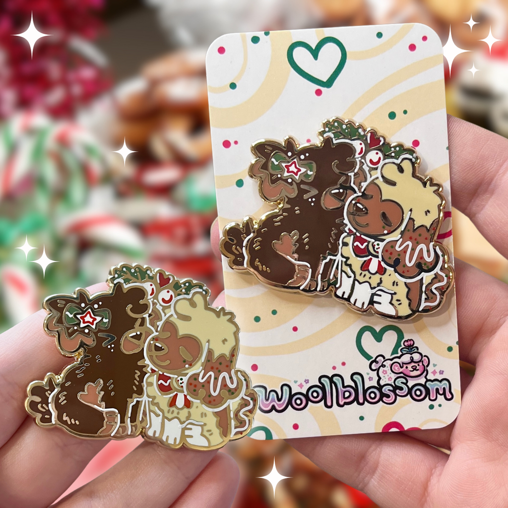 an enamel pin featuring Cinnamon, the Gingersnap puppy, and Caramel, the Sugar Cookie puppy, sharing a sweet mistletoe kiss