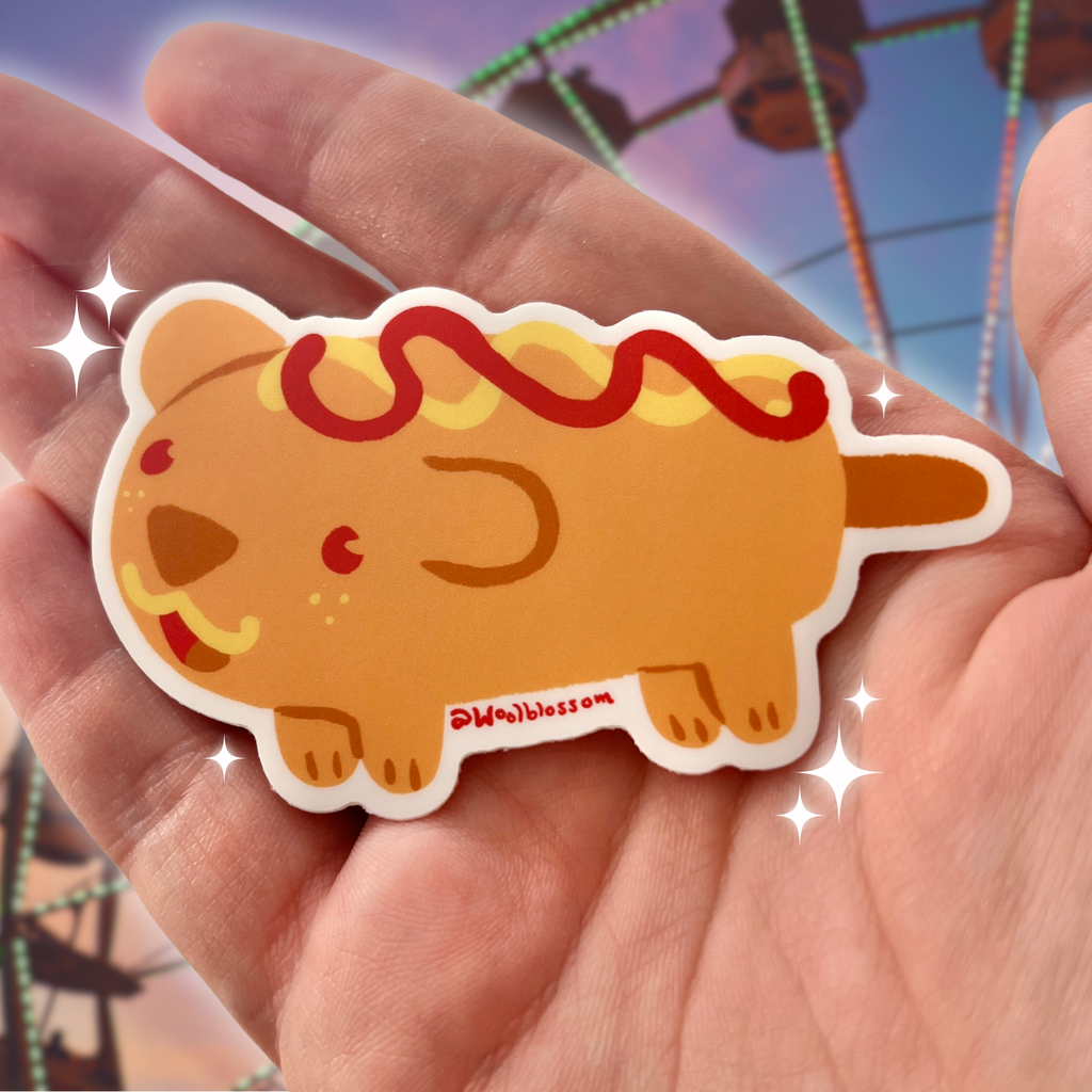Hand holding a cartoon corn dog sticker with a ferris wheel in the background