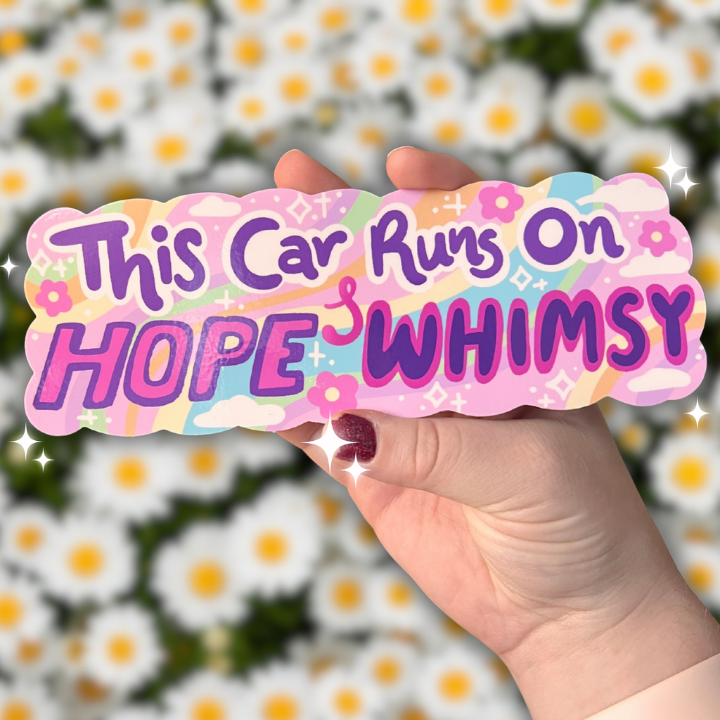 Hand holding a colorful bumper sticker with text 'This Car Runs On HOPE & WHIMSY' against a daisy flower background
