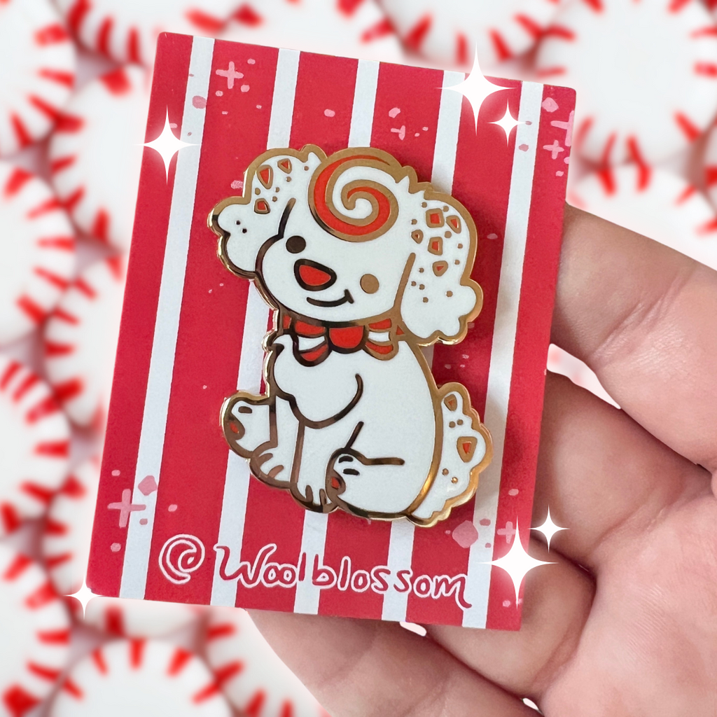 An golden enamel pin of candy the peppermint puppy, a white dog with fluffy ears and tail which have red peppermint bark spots. She has a red swirl forehead and red bow.