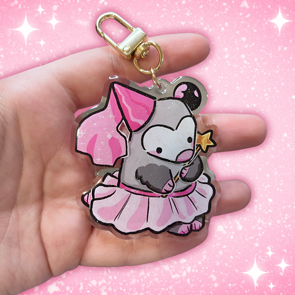 A charm of an opossum with a pink cone princess hat, tutu, and gold star wand