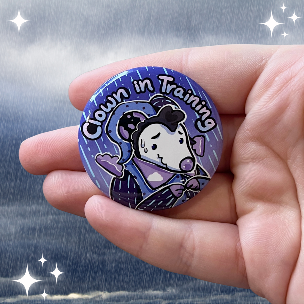 A button of a rain themed opossum that looks a little nervous with the text "clown in training"