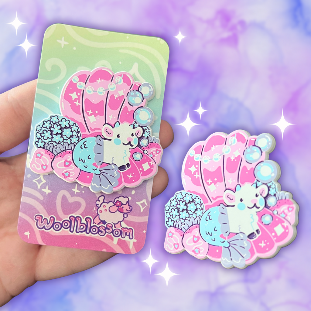 Enamel pin of a mermaid goat in a seashell on a colorful card held by a hand against a purple gradient background.