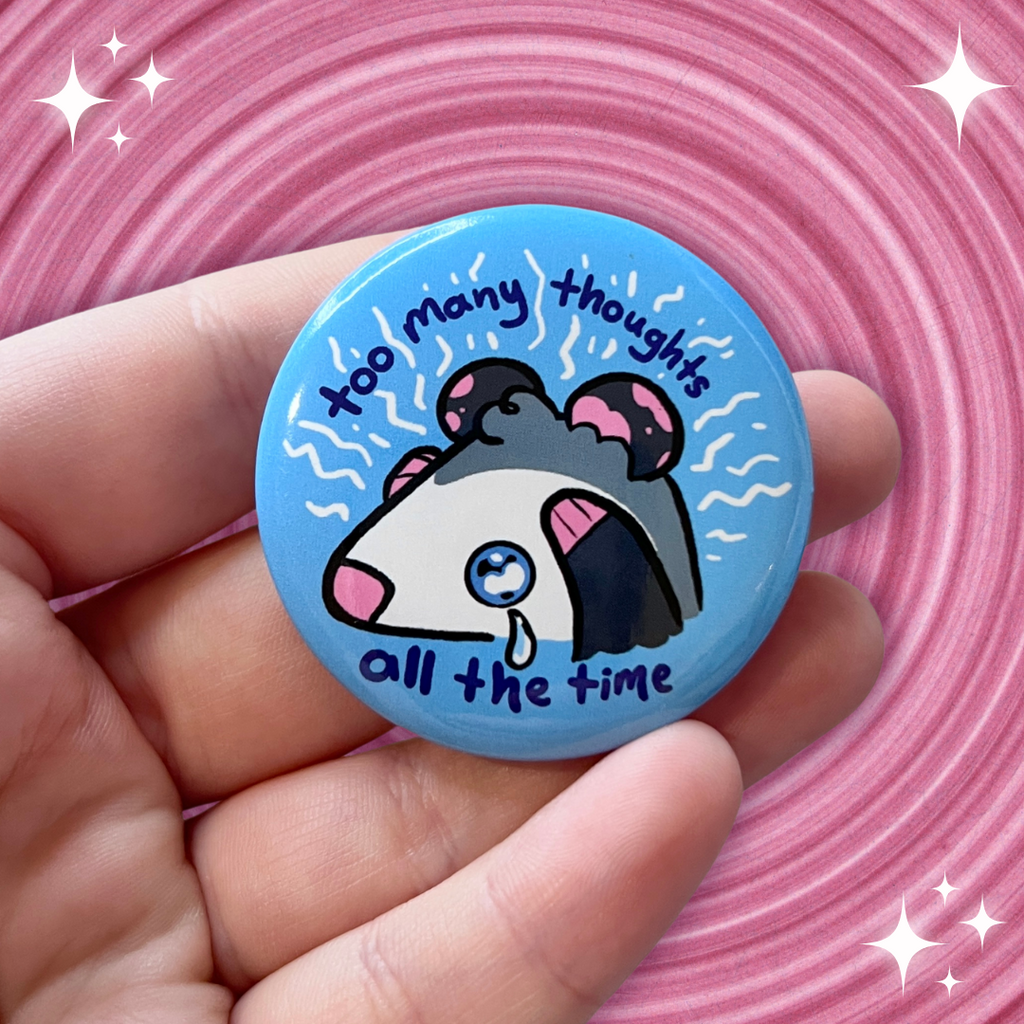 A blue button with an opossum gripping its forehead and electric lines coming up around it, with text that says "too many thoughts all the time"