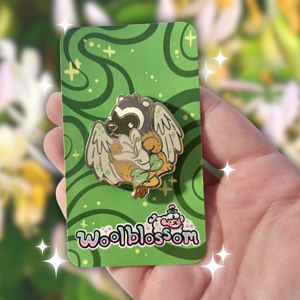 Hand holding a green card with an enamel pin of a badger gryffin holding a honeysuckle and 'Woolblossom' branding.