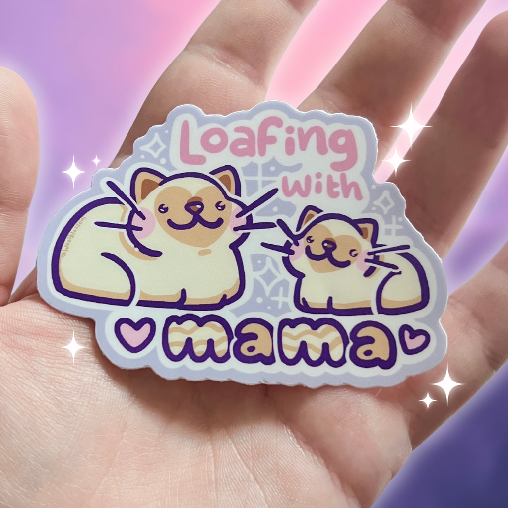 Sticker with cartoon cats and text 'Loafing with mama' held in a hand against a colorful background.