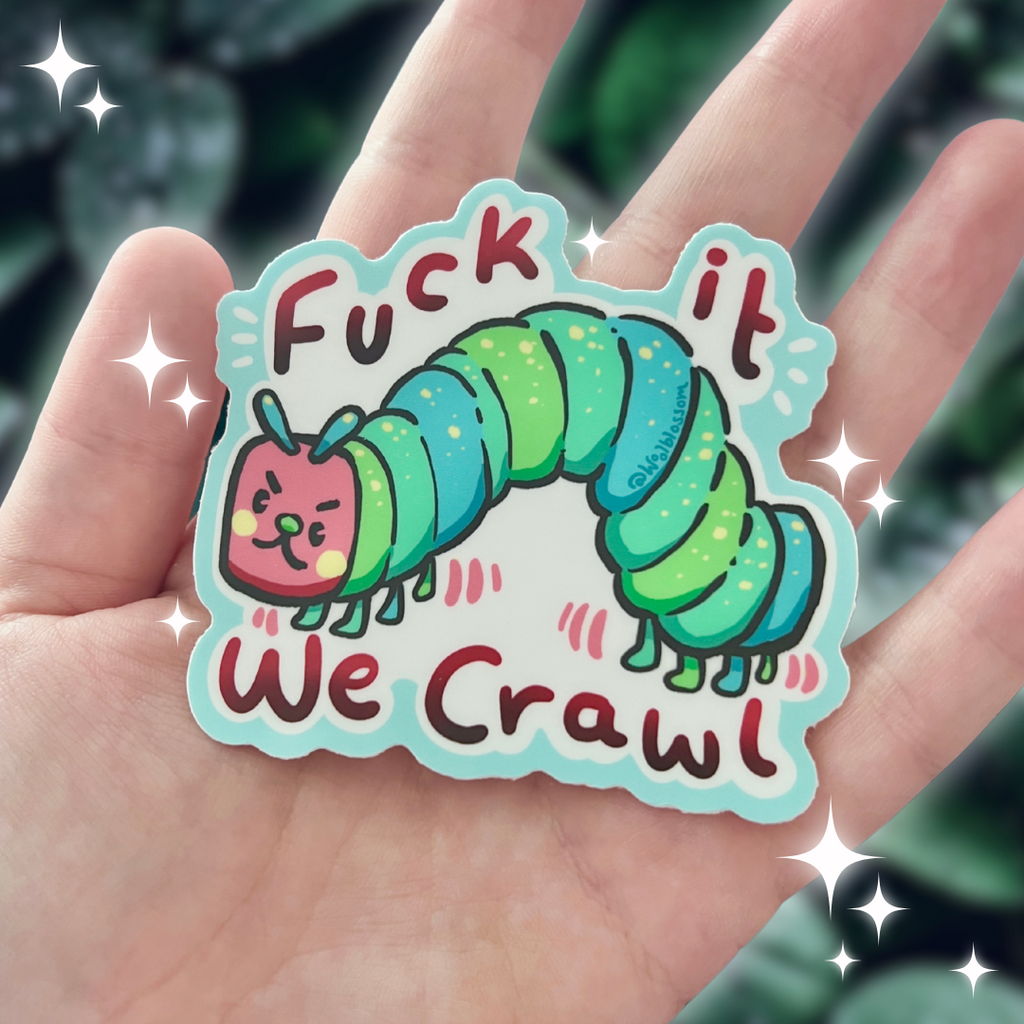 Sticker with a caterpillar design and text that says "fuck it we crawl" held in a hand against a blurred green background