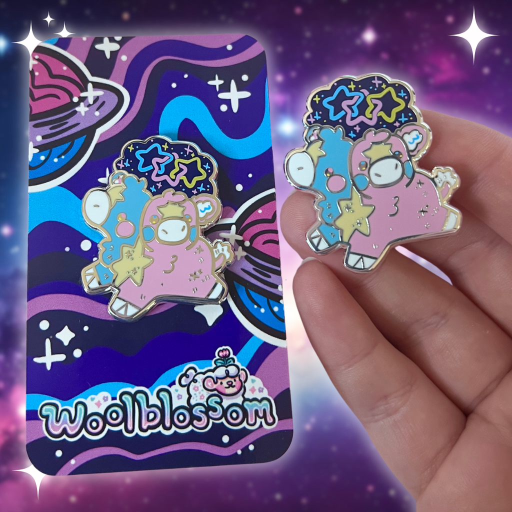 An enamel pin of a two headed calf, one is blue and one is pink, with a yellow star pattern connecting them and on each forehead. On top is a starry sky with three interlocking stars, one blue, one pink, and one yellow.