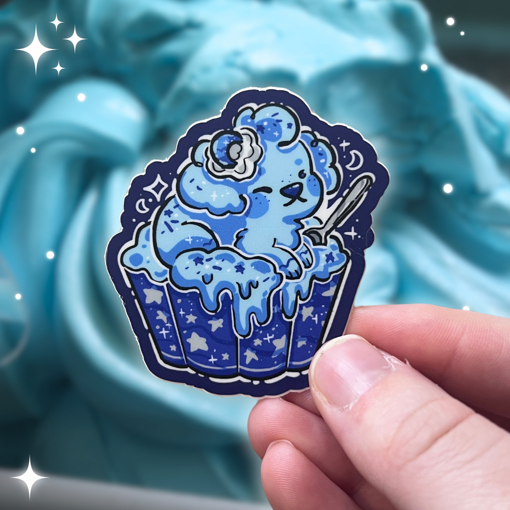 A sticker of a blue puppy in a cup of blue moon ice cream. The cup has silver color accents, and there are star sprinkles, with a general space vibe.