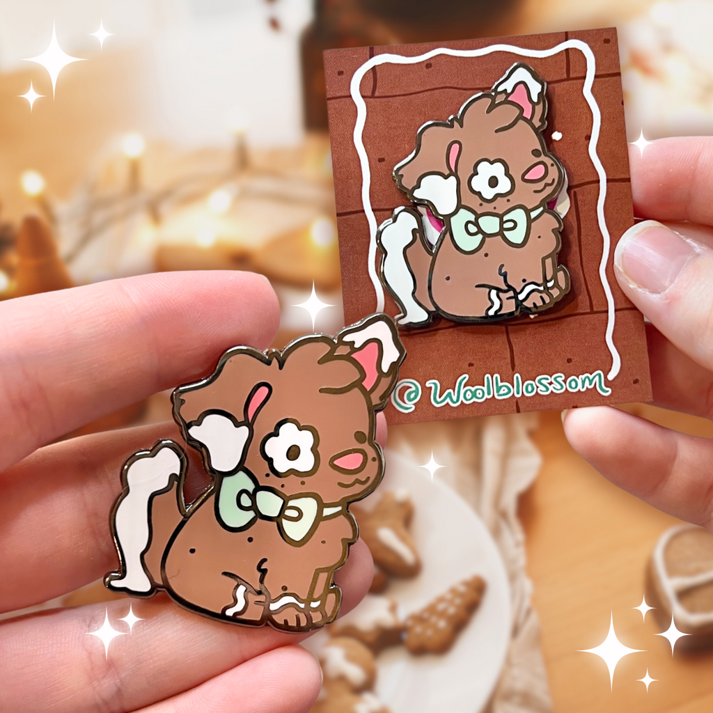 A black nickel enamel pin of Clove the gingerbread puppy, a brown puppy with white frosting accents on her ears and tail, as well as green bow.