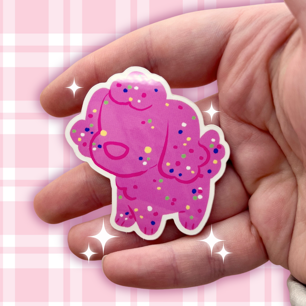 Hand holding a pink cartoon character sticker with colorful dots on a pink checkered background
