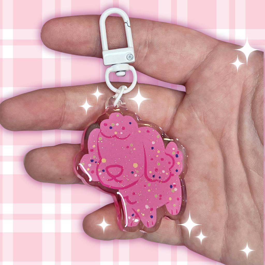 Pink cartoon character keychain held in a hand with a pink checkered background