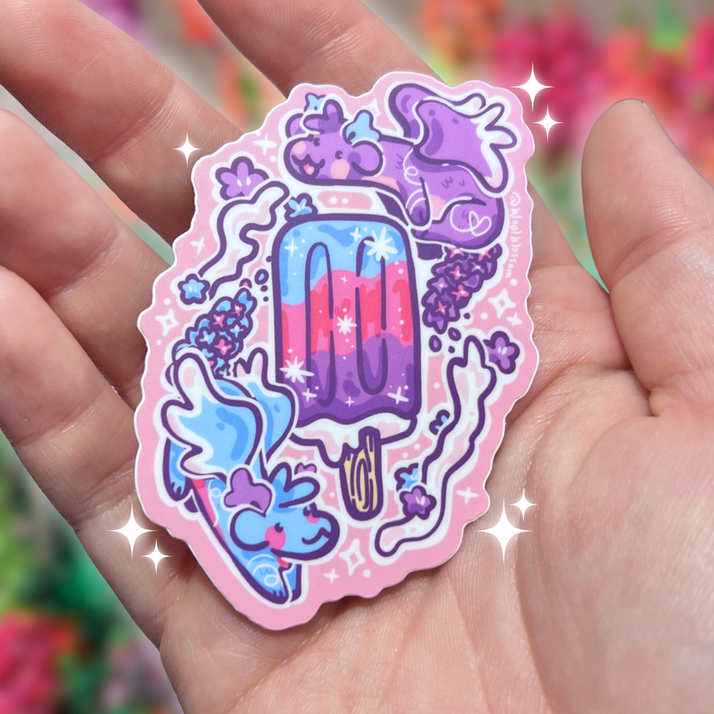 Hand holding a colorful sticker of two dragons flying around a popsicle against a blurred floral background