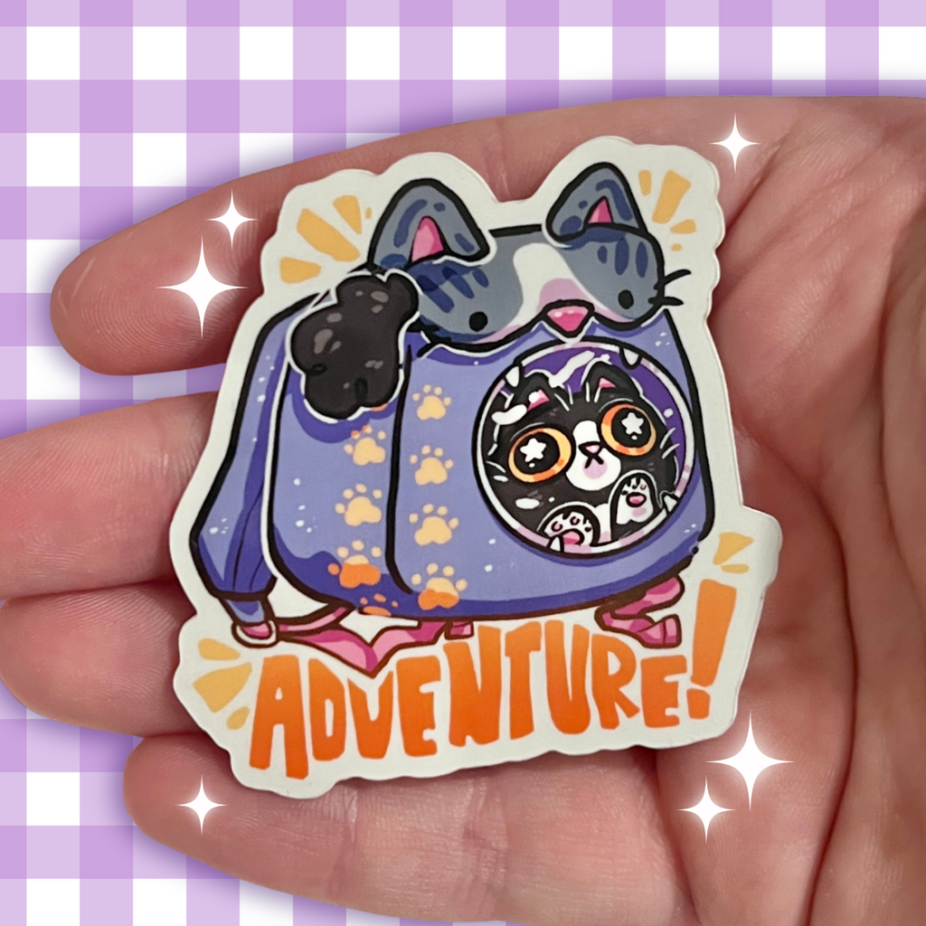Cartoon cat sticker with 'ADVENTURE!' text held in a hand against a purple checkered background