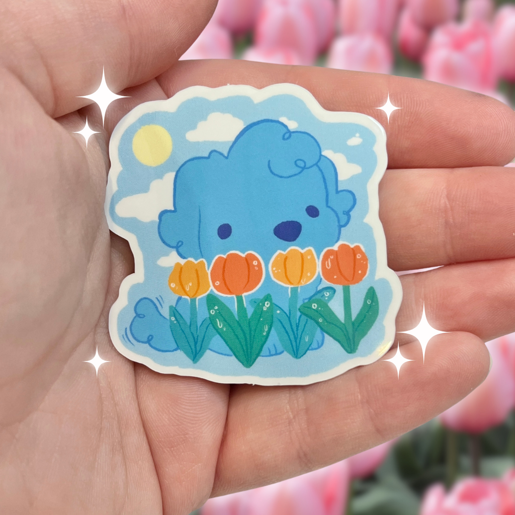 Hand holding a sticker of a blue puppy with orange flowers, with pink tulips in the background.
