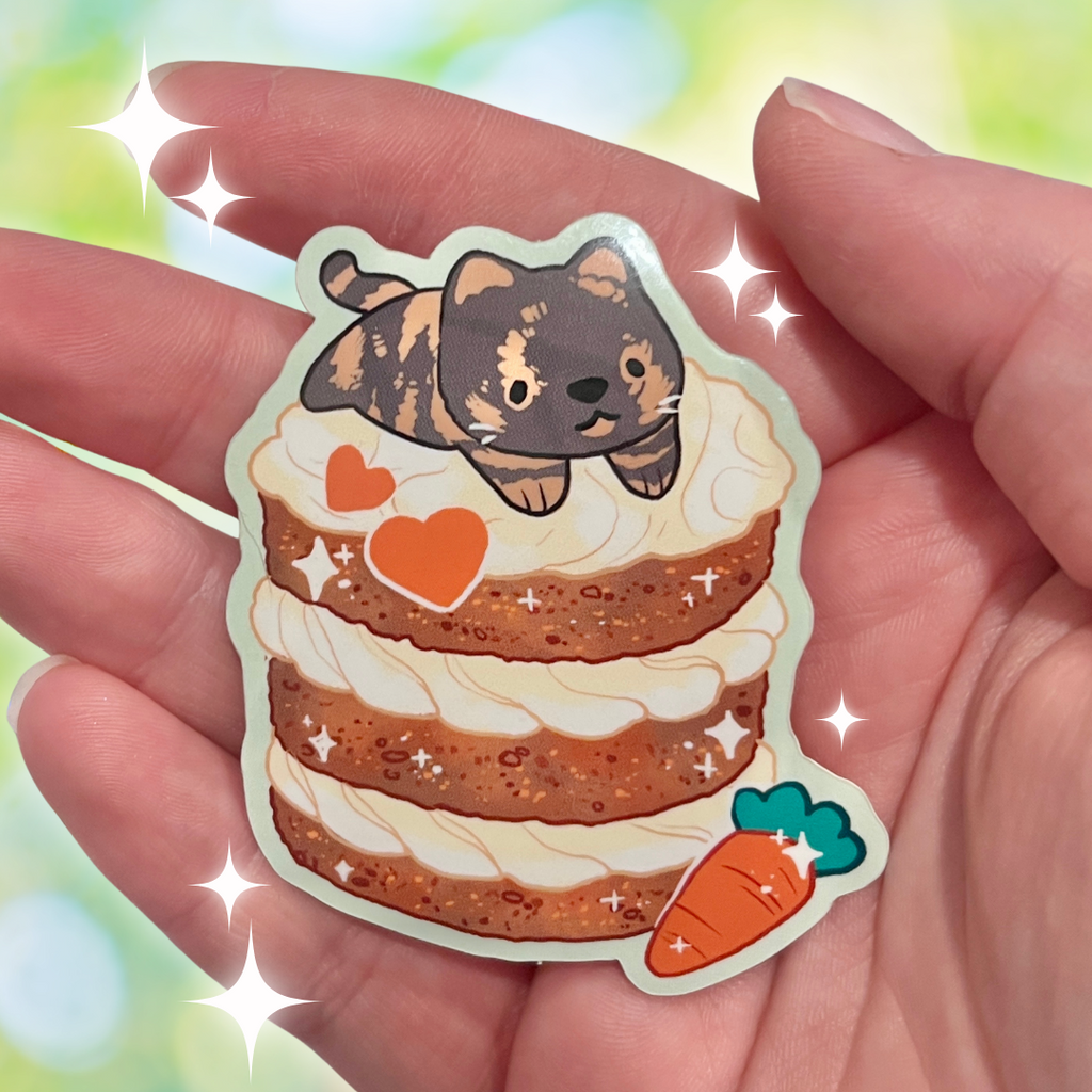 Sticker of a cat on a cake with hearts and carrots held in a hand against a colorful background.