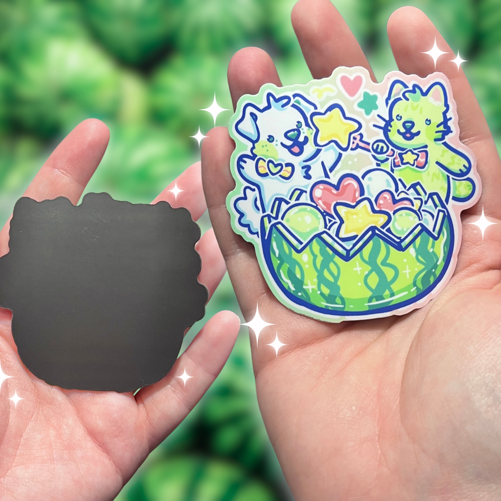 Colorful magnet of two cartoon character dog and cat eating a watermelon held in a hand with a green leafy background.