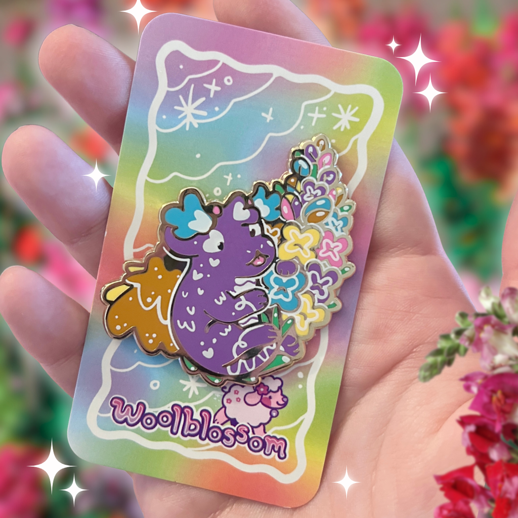 Colorful pin with a cartoon dragon holding its flower tail on a card held in a hand, surrounded by flowers.