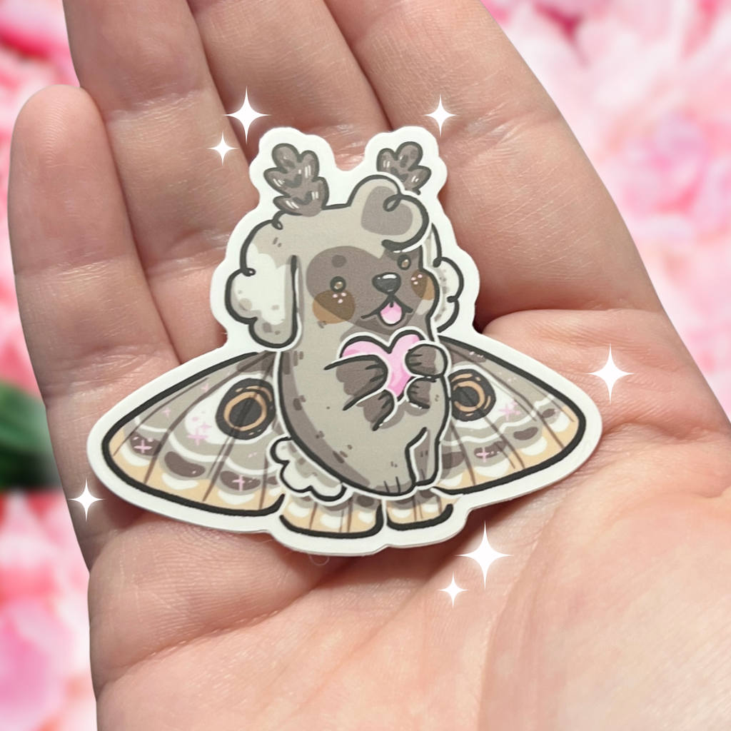 Cartoon moth puppy sticker held in a hand with a soft pink background