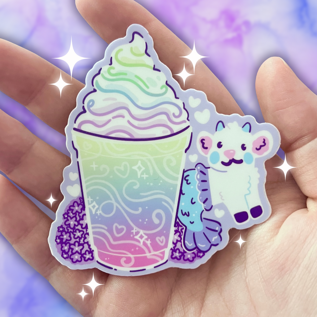 A colorful sticker of a rainbow-themed drink and mermaid goat held in a hand with a sparkly purple background.
