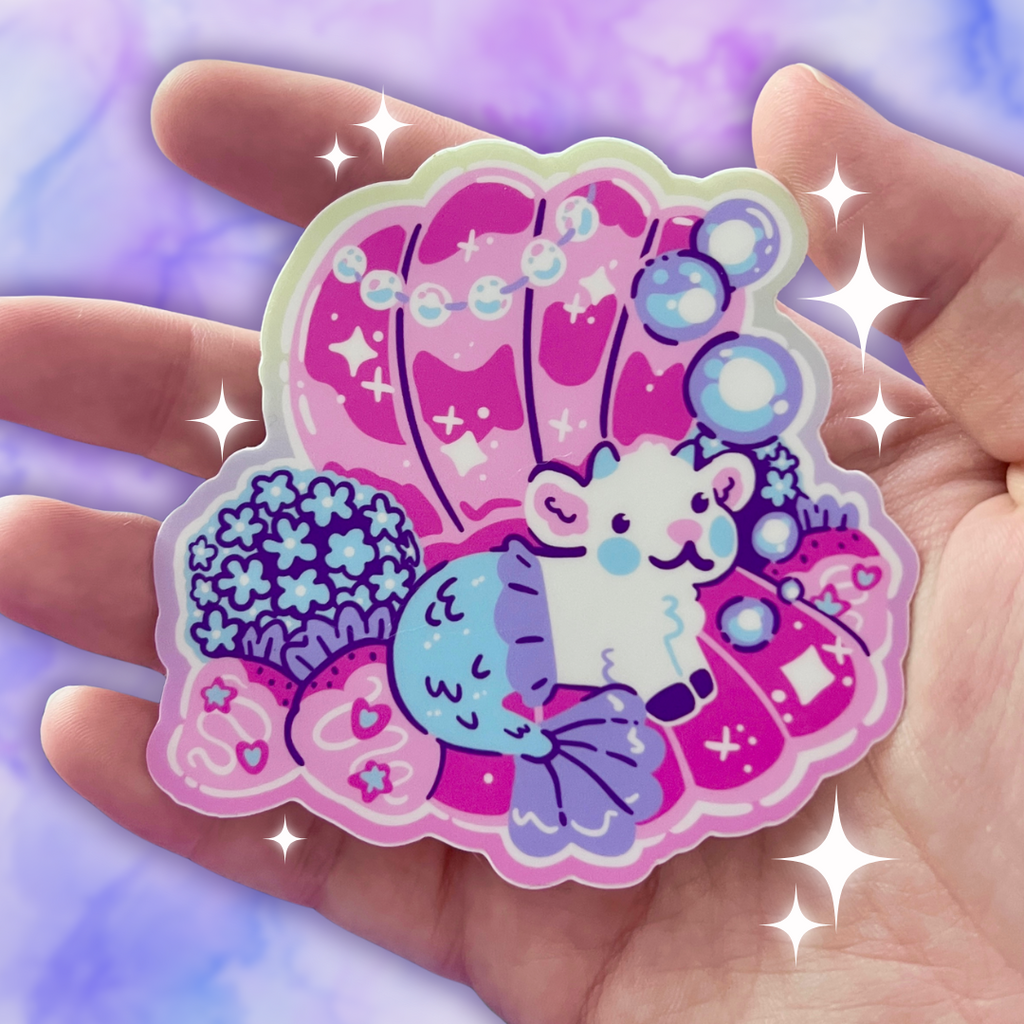 Colorful sticker of a mermaid goat in a pearl shell held in a hand with a sparkly background