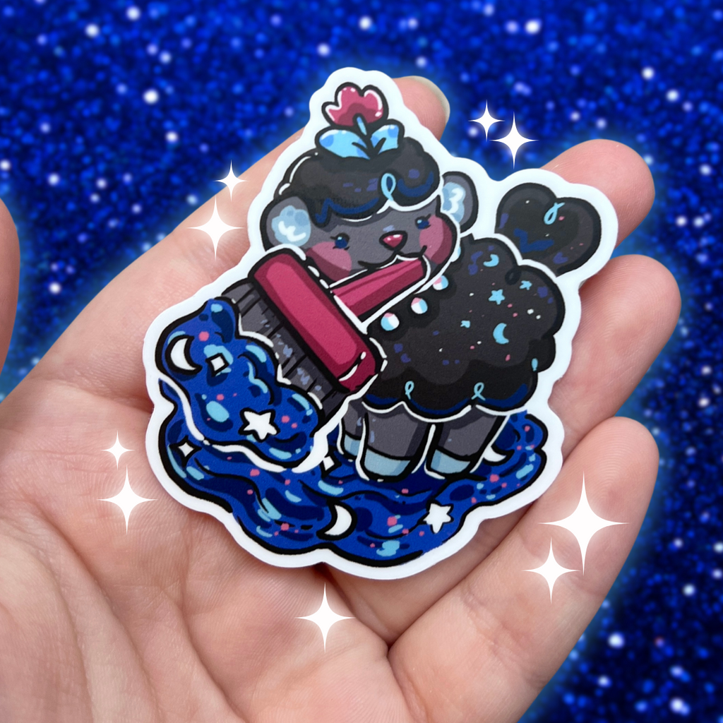 Cartoon character sticker of a sheep holding a paintbrush, held in a hand with a blue glittery background