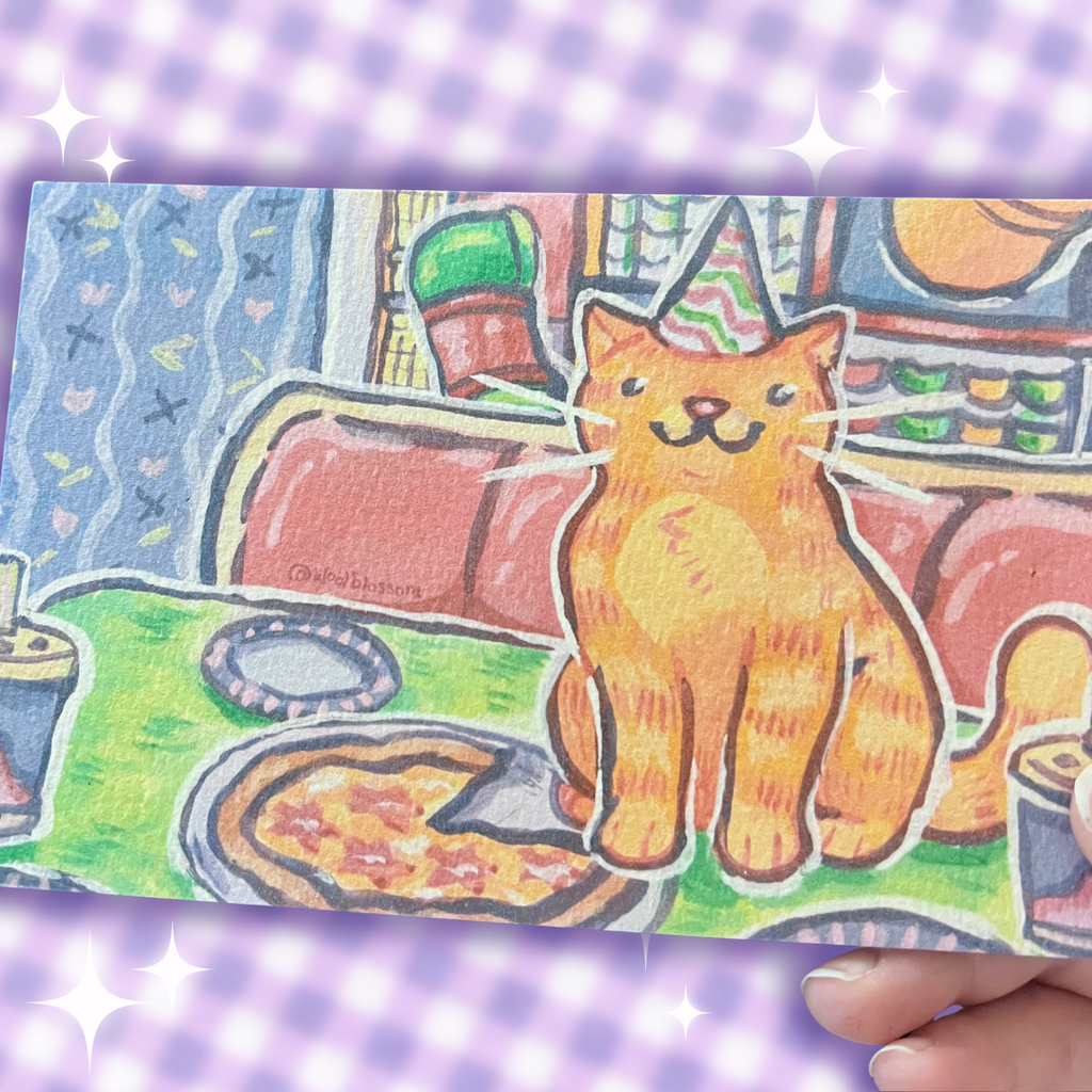 Hand holding a print of a cat with a party hat