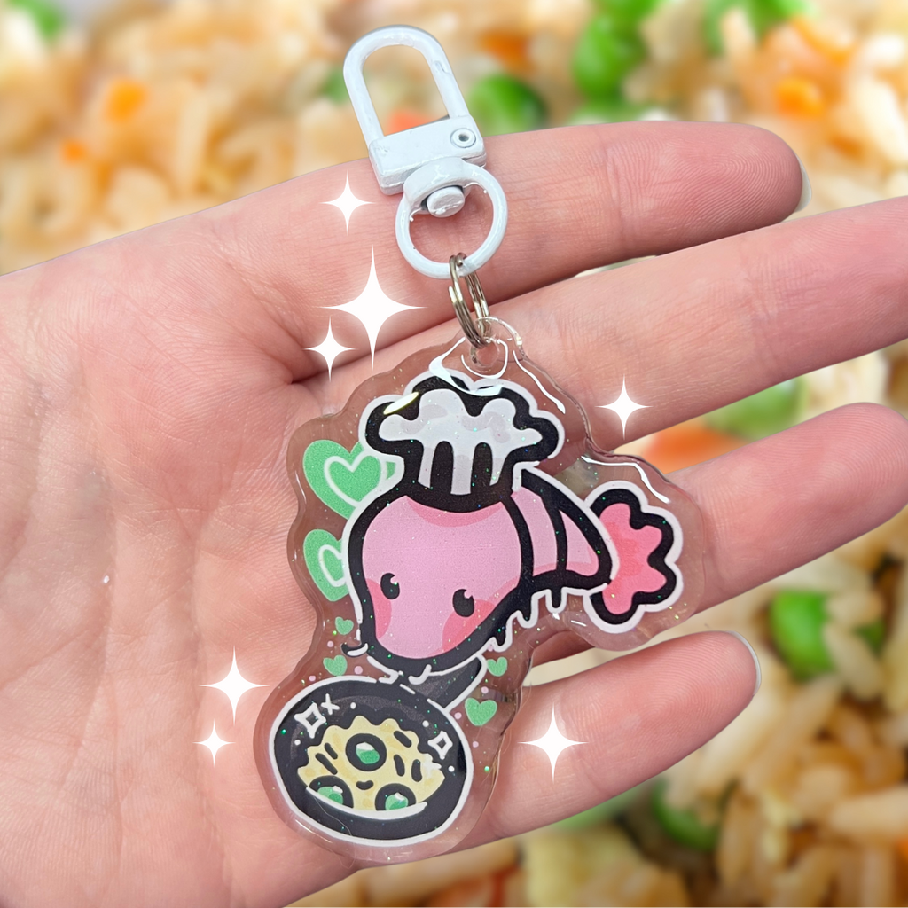 A keychain of a shrimp with a chefs hat holding a skillet of fried rice